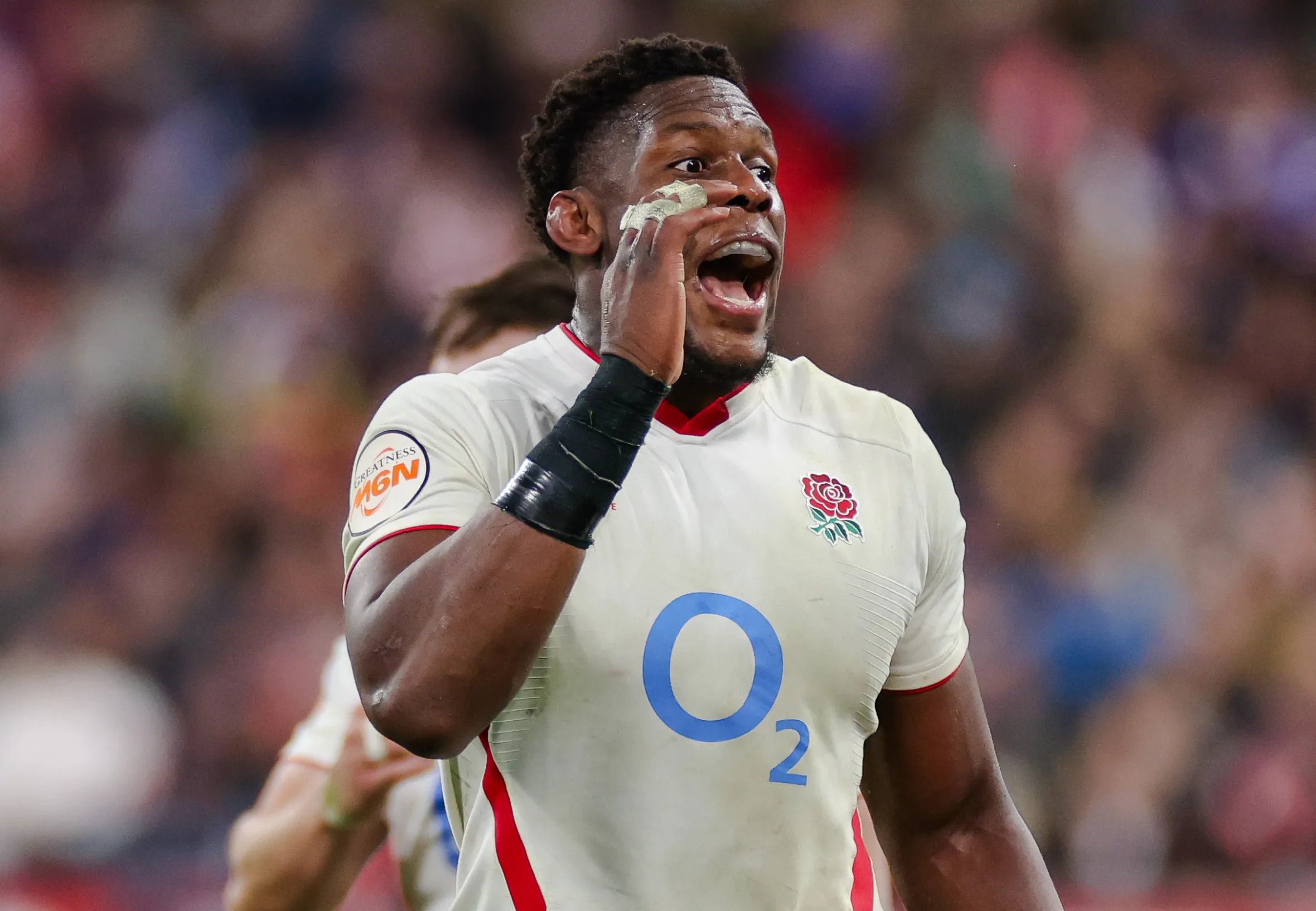 England's Maro Itoje wearing a white and red rugby uniform with a bandana on his arm, looks serious during the match.